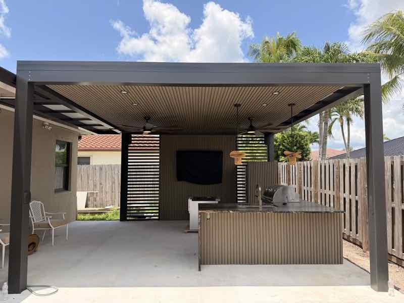 Attached flat-panel pergola with ceiling fans, TV, and built-in outdoor kitchen beside a Miami backyard patio