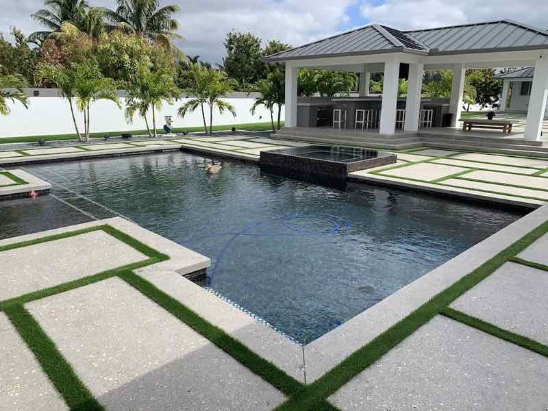 Rectangular pool with dark mosaic raised spa framed by a geometric turf-and-paver deck pattern