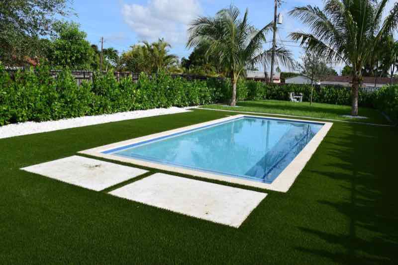 Rectangular pool bordered by artificial turf and a paver walkway