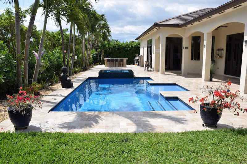 Wider view of a rectangular pool with raised spa and covered lanai beside a single-story home