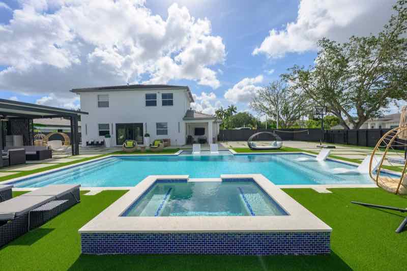 Large pool with raised spa, waterfall feature, turf deck, and hanging egg chairs