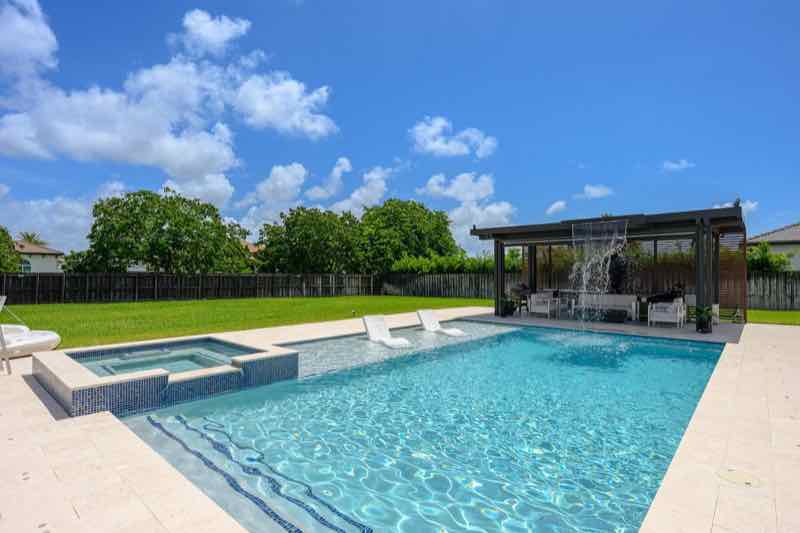 Pool with raised spa beside a pergola-covered outdoor kitchen and seating area
