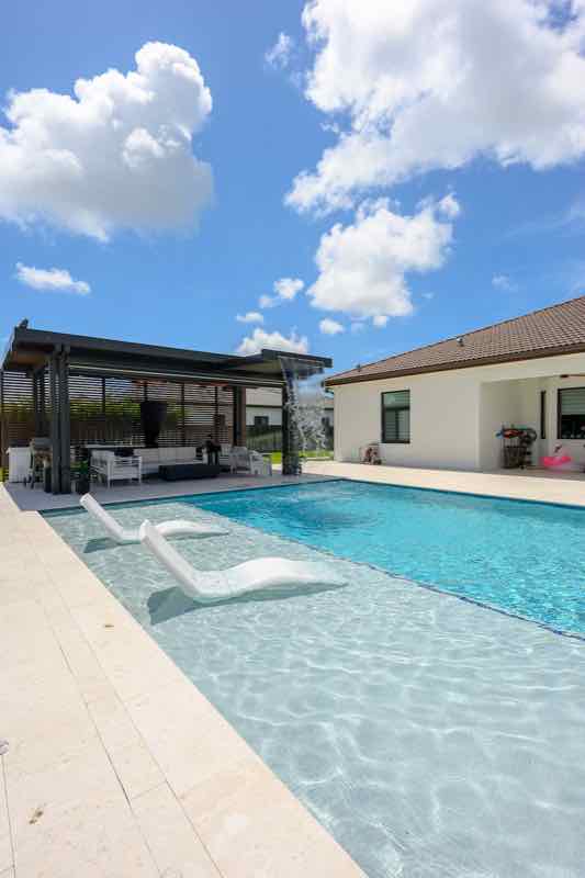 Angled view of a pool with a white in-pool tanning ledge beneath a pergola