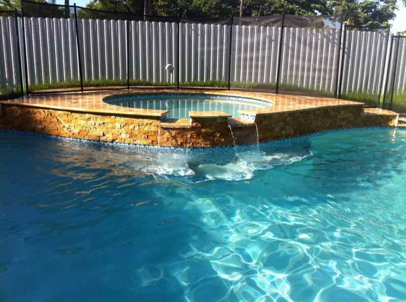Pool with a raised stone spa and waterfall spillover behind a privacy fence