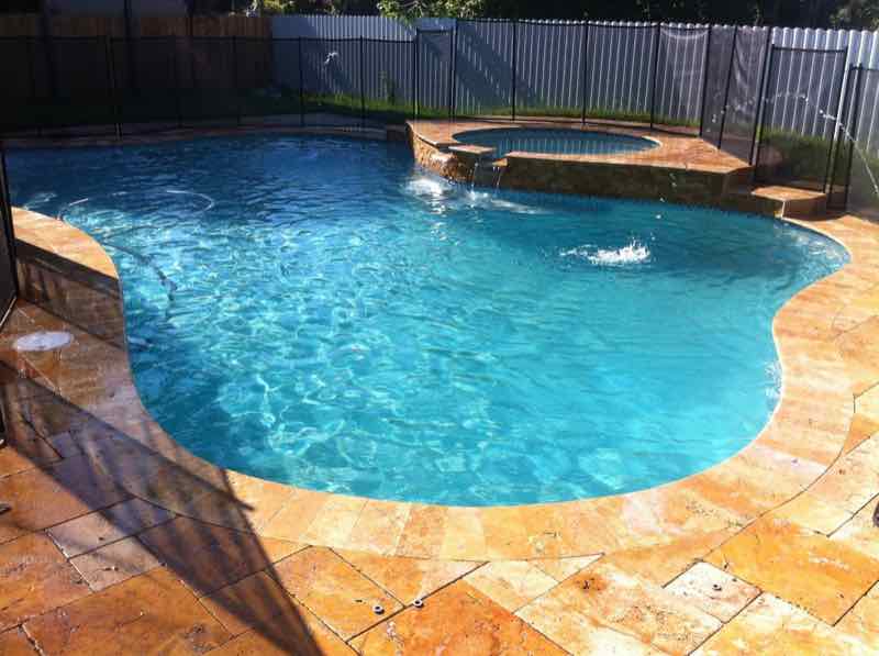 Freeform pool with raised spa and bubbling water feature on a travertine deck