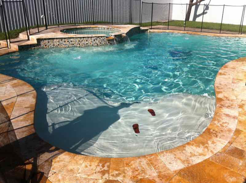 Freeform pool and raised spa with pool floats on a travertine deck behind a safety fence