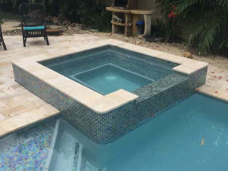Square raised spa with mosaic tile beside a stone patio and potted plants