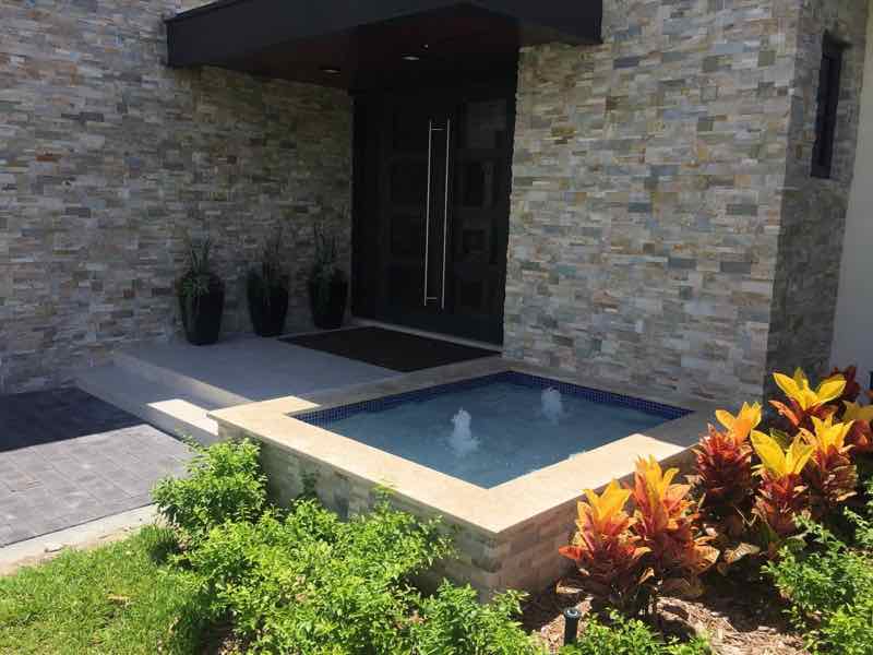 Small raised spa with waterfall spillover beside a modern stacked-stone entryway