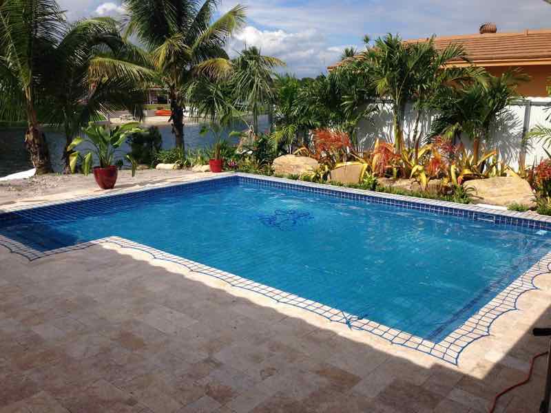 Rectangular pool with raised spa and fire-bowl accents beside a waterfront lawn