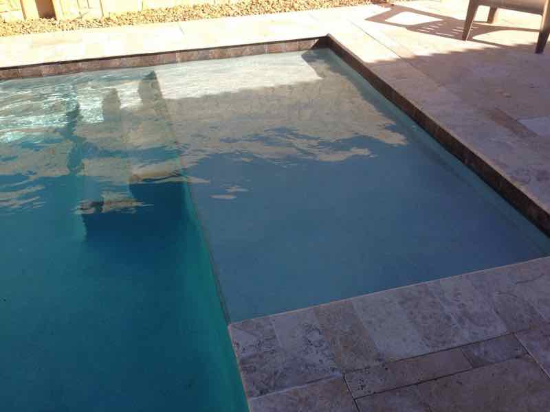Close-up of a pool's tanning ledge and travertine coping in late-day light