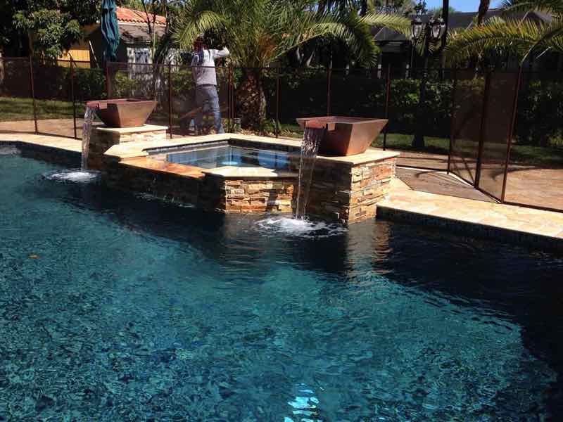 Rectangular pool with raised spa and dual water-jet fountains beside a screened enclosure
