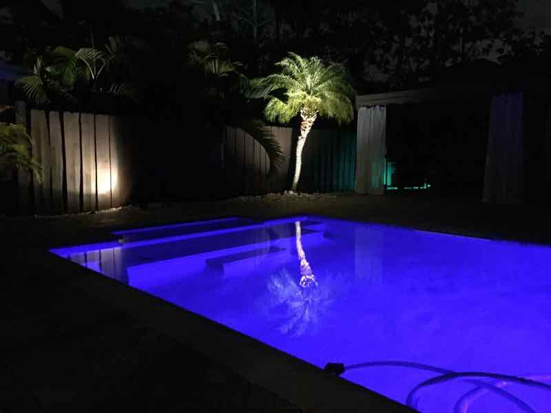 Rectangular pool lit blue at night beside a landscaped backyard