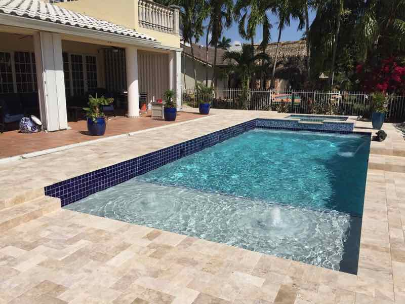 Rectangular pool with dark mosaic raised spa and bubbling jets on a travertine deck