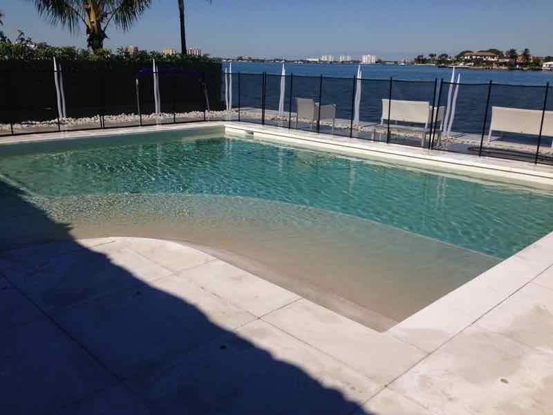 Rectangular pool with tanning ledge overlooking a waterfront canal behind a safety fence