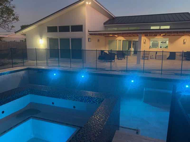 Rectangular pool and spa lit with blue LED lighting, viewed from above at dusk