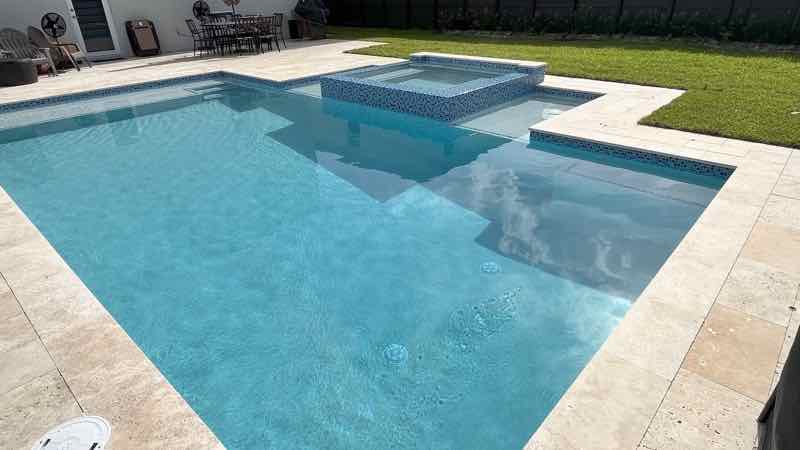 Rectangular pool with a squared tanning ledge on a travertine deck