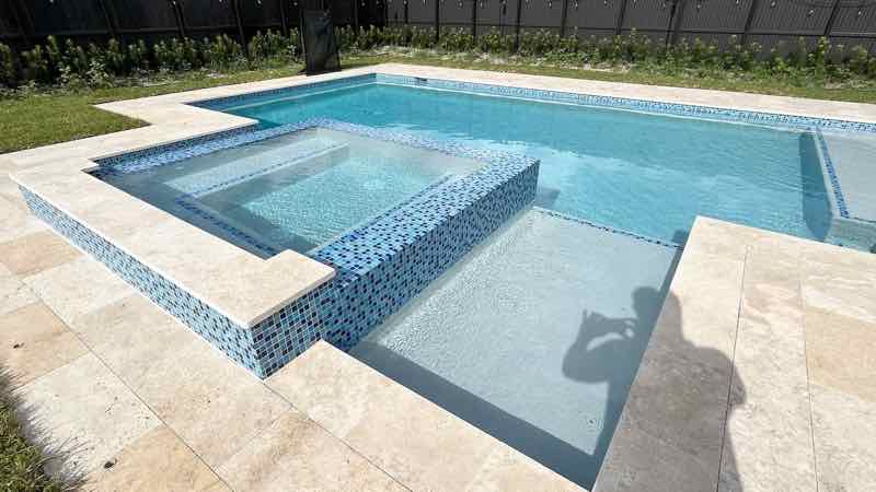Rectangular pool with raised mosaic-tile spa and step entry on a travertine deck