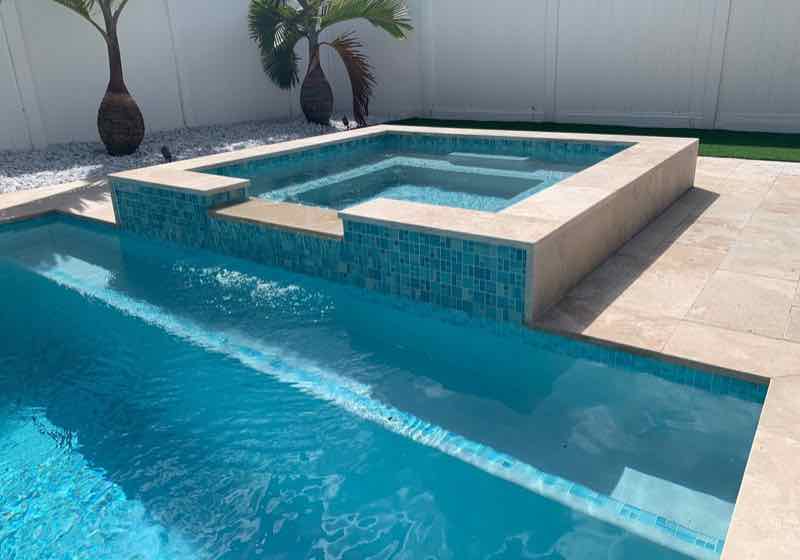 Rectangular pool with raised mosaic-tile spa and sun shelf on a travertine deck