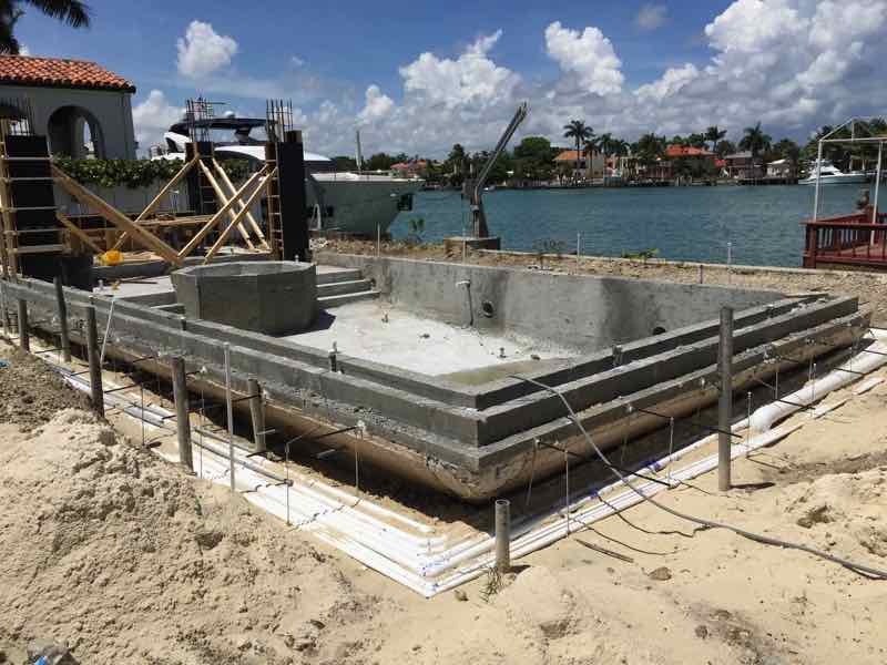 Pool shell mid-construction with rebar and formwork beside a waterfront lot