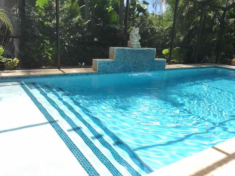 Rectangular lap pool with tanning-ledge tile striping and a stone water feature