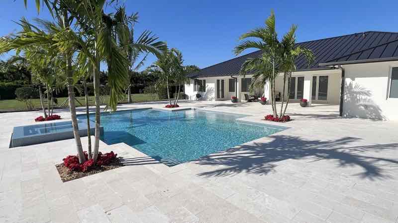 Freeform pool with raised spa beside a palm-shaded travertine patio
