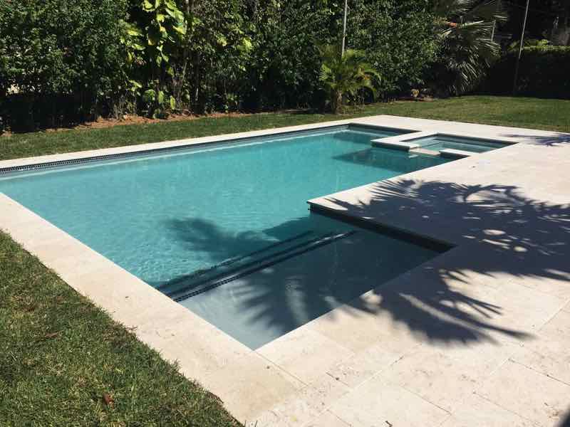 Rectangular pool with a squared tanning ledge and shade from a mature tree