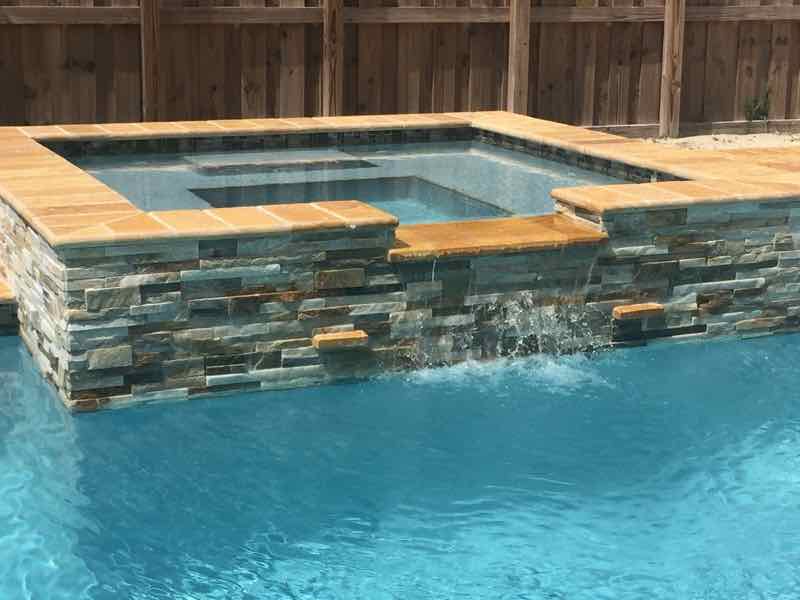 Raised stacked-stone spa with a sheer waterfall spilling into the pool below