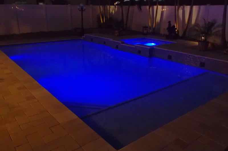 Rectangular pool and spa glowing blue at night on a brick-paver patio