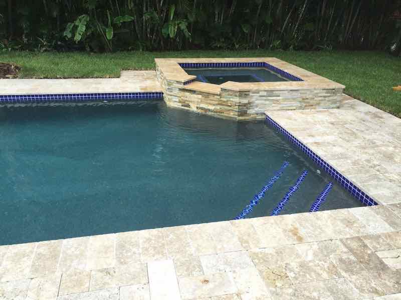 Rectangular pool with a step entry on a travertine deck at dusk