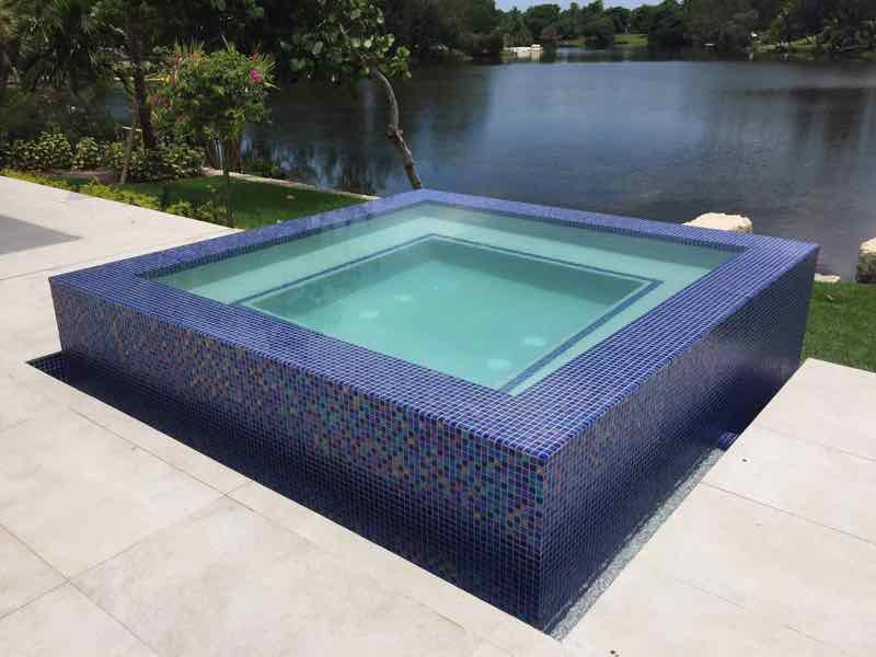 Raised mosaic-tile spa beside a lake, viewed from the deck corner