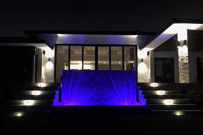 Illuminated purple LED waterfall feature spilling from a raised spa at night
