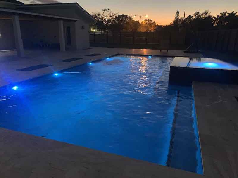 Rectangular pool with underwater and deck lighting glowing blue at sunset