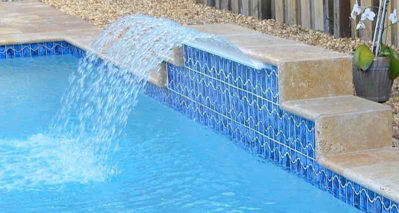 Raised mosaic-tile wall with a sheet waterfall cascading into the pool