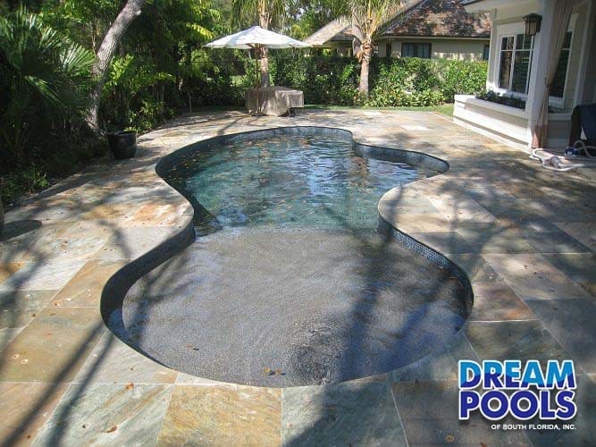 Freeform pool with tiled deck and tropical landscaping